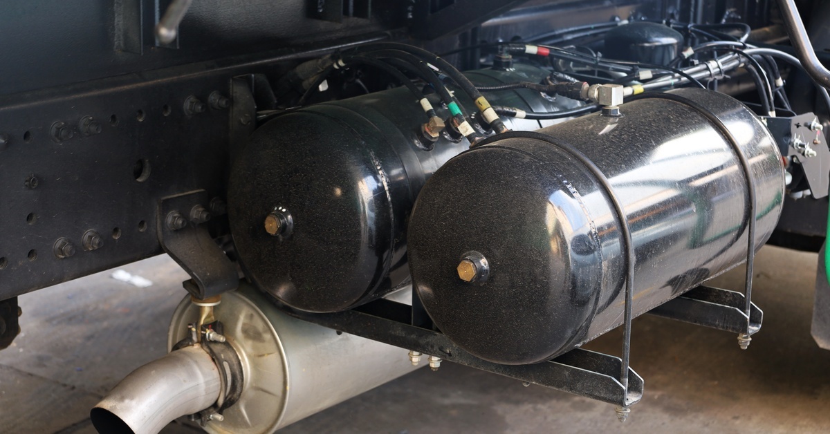 What Are DOT Fittings? DOT Fittings Explained Two black cylindrical air tanks for a brake system suspended on a rack, with tubing connected to brass fittings.