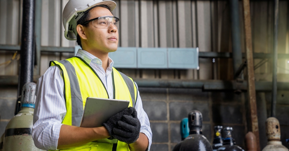 Signs Your Compressed Air Tank Needs Replacement An industrial worker in a hard hat, safety vest, and gloves holds a tablet while standing in front of air receiver tanks.