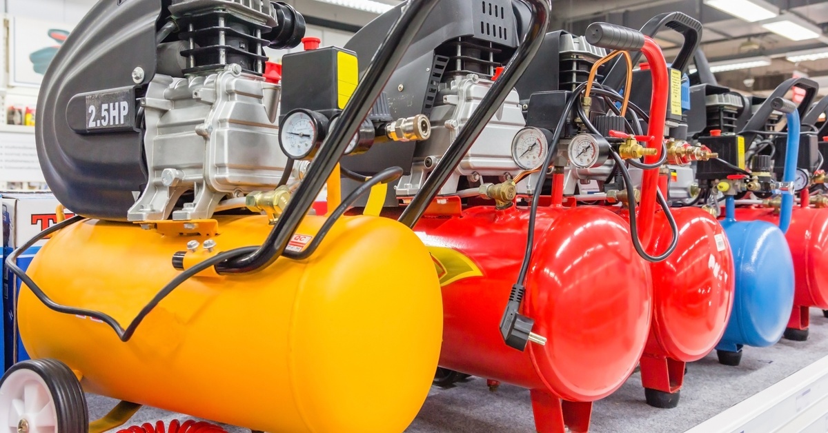 Signs Your Compressed Air Tank Needs Replacement Various colored horizontal air compressor tanks, including yellow, red, and blue, lined up in a warehouse.